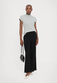 Top grigio chiaro a maniche corte con collo alto, abbinato a pantaloni neri a gamba larga. Gli accessori includono una piccola borsa nera e scarpe bianche.