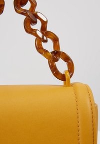 Sac à main en cuir jaune avec une chaîne en écaille de tortue brillante. Il présente une silhouette arrondie et des coutures visibles le long des bords.
