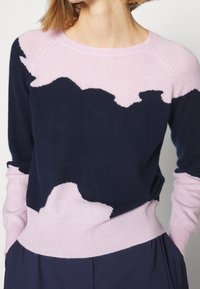 Pull en navy et rose avec un tricot doux et texturé. Présente des motifs en vagues sur la poitrine et les manches, ainsi qu'un ourlet ajusté.