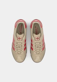 Μπεζ αθλητικά παπούτσια με κόκκινες ρίγες, υφασμάτινη επάνω επιφάνεια με υφή, στρογ�γυλή μύτη και σχέδιο με κορδόνια. Περιλαμβάνει λογότυπο στη γλώσσα και μαλακή επένδυση.