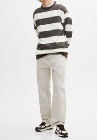 Sudadera a rayas grises y blancas con cuello redondo, combinada con pantalones beige claro de pierna recta y zapatillas negras y blancas.