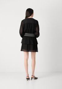 Black tiered dress with pleated fabric, sheer long sleeves, elastic waistband with intricate detailing, and above-the-knee length.