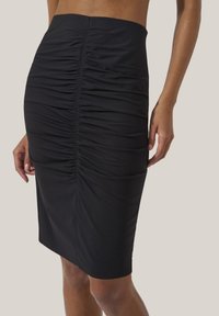 Svart figurnära kjol med rynkad textur som löper vertikalt, knälång, och med en slät tygfinish som framhäver kroppens konturer.