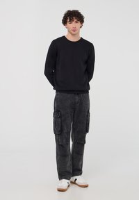 Felpa nera, vestibilità comoda, scollo a costine. Pantaloni cargo grigi con più tasche, texture sbiadita. Sneakers bianche con dettagli neri.