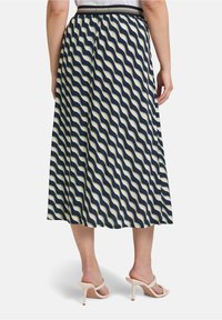 Jupe maxi crème avec un motif ondulé bleu marine. Taille élastique, tissu lisse, et longueur pleine jusqu'aux chevilles. Assortie à des talons nude.