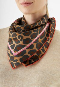 Leopardprint zijden sjaal in bruin, zwart en oranje, met een roze geometrische streep en rode rand. Om de nek gedrapeerd.