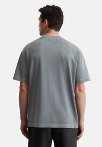 T-shirt gris à manches courtes avec une coupe décontractée, fabriqué en coton doux. Il possède un col rond et des ourlets cousus, avec une étiquette près de la couture latérale.