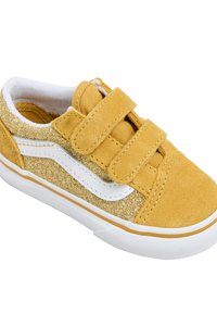 Zapatilla de ante amarilla con un acento dorado brillante, línea lateral blanca y dos correas de gancho y bucle; suela de goma texturizada.