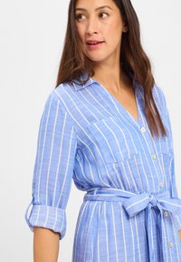 Blue striped dress with long sleeves, button-down front, two chest pockets, and a tied belt at the waist. Textured fabric with vertical stripes.
