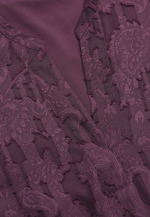 Lila Stoff mit einem strukturierten Muster aus floralen und geometrischen Designs, überlagert mit glattem Material, das Tiefe und Kontrast schafft.