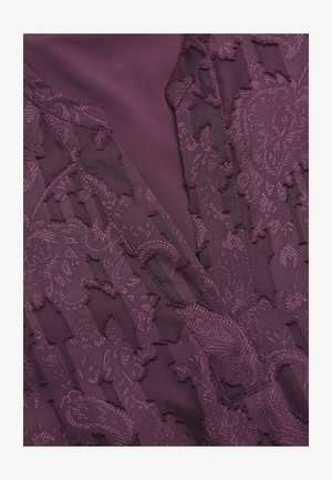 Violetti kangas, jossa on kukka- ja geometrisia kuvioita sisältävä teksturoitu pinta, kerrostettuna sileän materiaalin kanssa, luoden syvyyttä ja kontrastia.