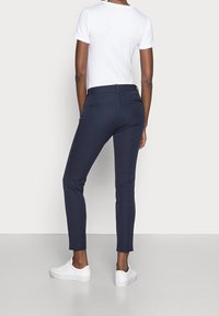 Navy fitted trousers with a smooth texture, two back pockets, and a low-rise waistband, paired with a plain white t-shirt and white sneakers.