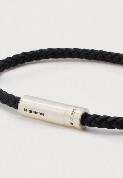 Fekete fonott bőrszíj ezüst hengeres záróval, amelyen a "le gramme" felirat és a "925" tisztasági jel van gravírozva.