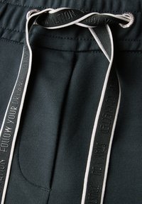 Mörkgröna mjukisbyxor med elastisk midja, med en dekorativ snörning och en sidoficka. Slät tyg med kontrasterande detaljer.