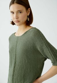 Grüner Strickpullover mit weitem Ausschnitt, Drei-Viertel-Ärmeln und strukturiertem Muster entlang der Mitte und der Ärmel.