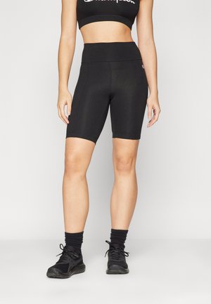 Shorts de sport noirs en tissu extensible, dotés d'une taille haute et d'une texture lisse. Portés avec un crop top noir assorti et des baskets.