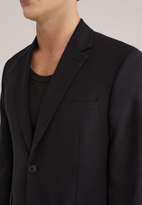 Črn krojen blazer iz gladkega blaga, z izrezanim ovratnikom, gumbom za zapiranje in subtilnim detajlom žepa na prsih.