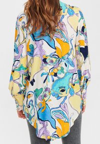 Blusa colorida y estampada con diseños abstractos en púrpura, azul, amarillo y verde. Mangas largas y dobladillo curvado; tejido ligero.