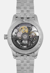 Automatyczny zegarek ze stali nierdzewnej z przezroczystym deklem, w którym widać misternie wykonane mechanizmy, złote akcenty oraz grawerunek "5 ATM WODOODPORNY".