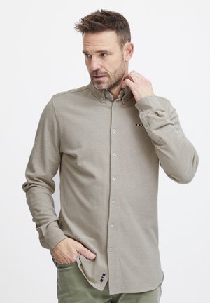 Lys beige langermet skjorte med knappestolpe og myk tekstur. Har en knepping-kollare og et lite stripet accent nær hakken.