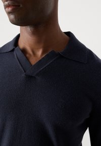Navy blue knit polo sweater with a V-neck design, featuring a textured fabric and subtle logo detail on the chest.
