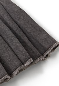 Tela plisada de color gris oscuro con textura visible y bordes deshilachados sobre un fondo blanco.