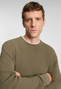 Rippstrick, olivgrüner Pullover mit langen Ärmel und rundem Ausschnitt. Subtil strukturiertes Muster mit einem V-förmigen Detail auf der Brust.