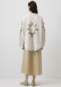 Bluză crem cu broderie complexă într-un model floral, asortată cu o fustă bej, evidențiind o siluetă relaxată și o textură moale a țesăturii.