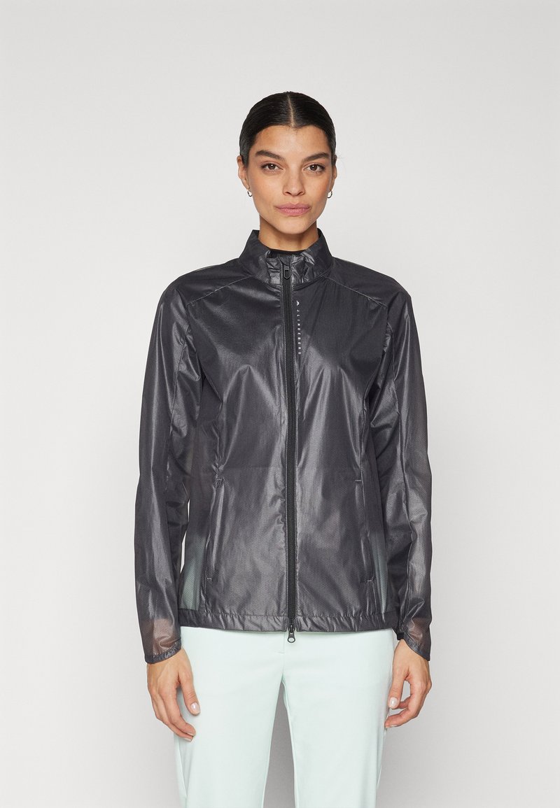 Svart, lätt vindjacka med hög krage, full dragkedja fram och långa ärmar. Har en slät, glänsande yta och minimal detaljering.