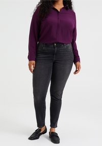 Lila långärmad skjorta med knappar i kombination med mörka tajta jeans och svarta slip-on skor, med en slät yta och en åtsittande design.