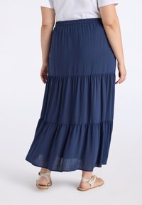 Gonna maxi a strati di colore blu navy realizzata in tessuto leggero; presenta una vita elastica e un orlo fluido. Indossata con sandali beige.