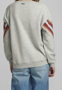 Sweat-shirt gris avec des accents côtelés en rouille, bleu et beige sur les manches. Fini avec un col rond et une coupe décontractée.