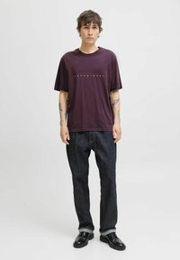 Bordo pamučna majica s bijelim natpisom "JACK & JONES". Uparena s tamnoplavim trapericama i crnim kožnim cipelama. Jednostavan dizajn, opušteni kroj.
