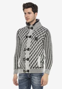 Gebreide cardigan in zwart en wit met een visgraatpatroon, hoge kraag, sluitingen met knoppen en twee voorzakken.