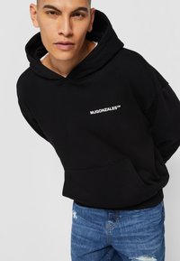 Sweat à capuche noir avec poche avant et logo blanc "MJGONZALES™". Assorti avec un jean en denim bleu usé. Texture de tissu lisse.