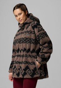 Giacca in pile marrone e nera con motivo, dotata di cappuccio, chiusura con zip, tasche laterali e vestibilità ampia. Logo del marchio visibile sul petto.