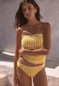 Bandeau bikinitop v rumeno-belih črtah z teksturirano tkanino, v paru z ujemajočimi se nizkimi bikini hlačkami. Gladek, raztegljiv material.