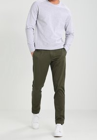 Grå långärmad sweatshirt med ribbad nederkant, kombinerad med olivgröna byxor och vita sneakers. Enkelt design, material i bomullsblandning, avslappnad passform.