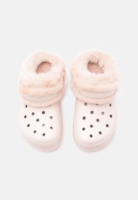 Rózsaszín műanyag klumpák puha, bolyhos szegéllyel. Szellőzőlyukakkal és sima felszínnel rendelkeznek, a kényelem és viselhetőség érdekében tervezve.