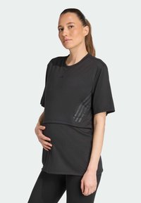 Sort atletisk t-shirt med korte ærmer, designet til graviditet. Har en panel med tre striber på siden, lavet af blødt stof.