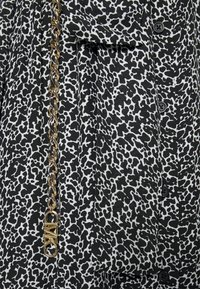 Svartvitt blus med leopardmönster, med en guldkedja som accent och svarta knappar framtill. Mjuk tygtextur.