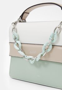 Struktureret håndtaske med hvide, beige og mintgrønne paneler. Har en kraftig mintgrøn kædehank og sølvfarvede hardware-detaljer.