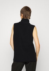 Černý bezrukávový rolák s ribbovanou strukturou a bočními rozparky, s vysokým límcem a volným střihem.