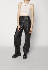 Svarta byxor i konstläder med vida ben och en ljusrosa kortärmad topp med en liten svart logotyp. Cirkulära svarta plattformsstövlar fulländar looken.