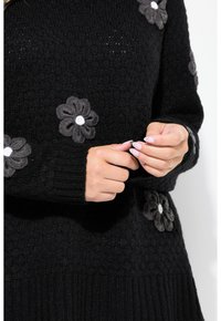 Mustat neulotut neuleet, joilla on teksturoitu kangas; siinä on harmaita kukka-applikaatioita, joissa on valkoiset keskiosat. Ribbausvahvistettu hihansuu ja helma.