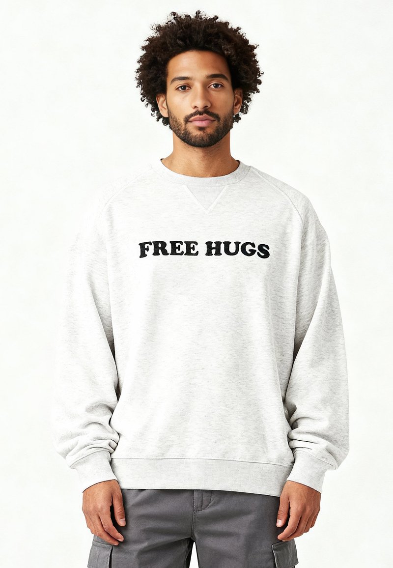 Sweat-shirt gris avec texte noir "FREE HUGS", doté d'un col rond et de poignets côtelés. Confectionné dans un tissu doux et texturé. Coupe décontractée.