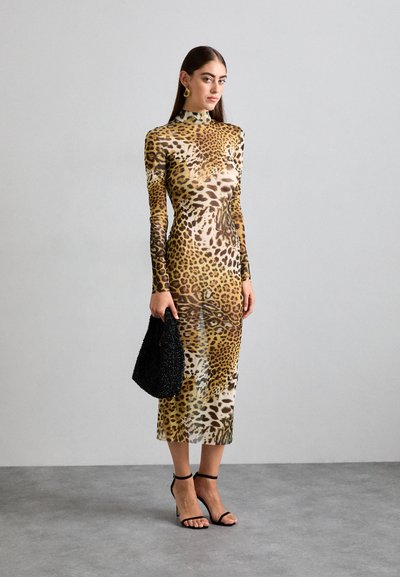 Long-sleeve, form-fitting dress in a leopard print pattern. Sheer fabric with a high neck and mid-calf length. Black handbag and strappy heels.