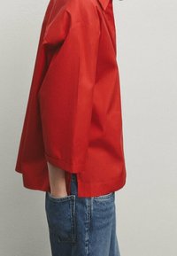 Camicetta rossa a maniche corte realizzata in tessuto liscio, con colletto e vestibilità comoda. Abbinata a jeans in denim blu.
