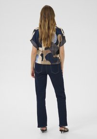 Majica s kratkimi rokavi z abstraktnim vzorcem v temnih barvah, v kombinaciji s temnimi kavbojkami. Obleko dopolnjujejo črne pete.