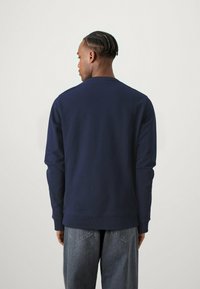 Felpa blu navy realizzata in materiale morbido, con colletto a girocollo e orlo a costine. Il retro presenta un design semplice senza loghi visibili.